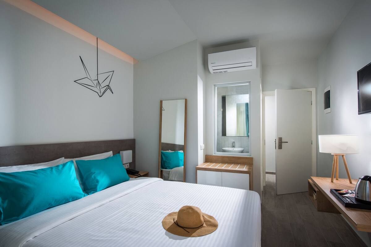 Ett hotellrum med en säng, ett skrivbord med en lampa, en spegel och en luftkonditioneringsanläggning.