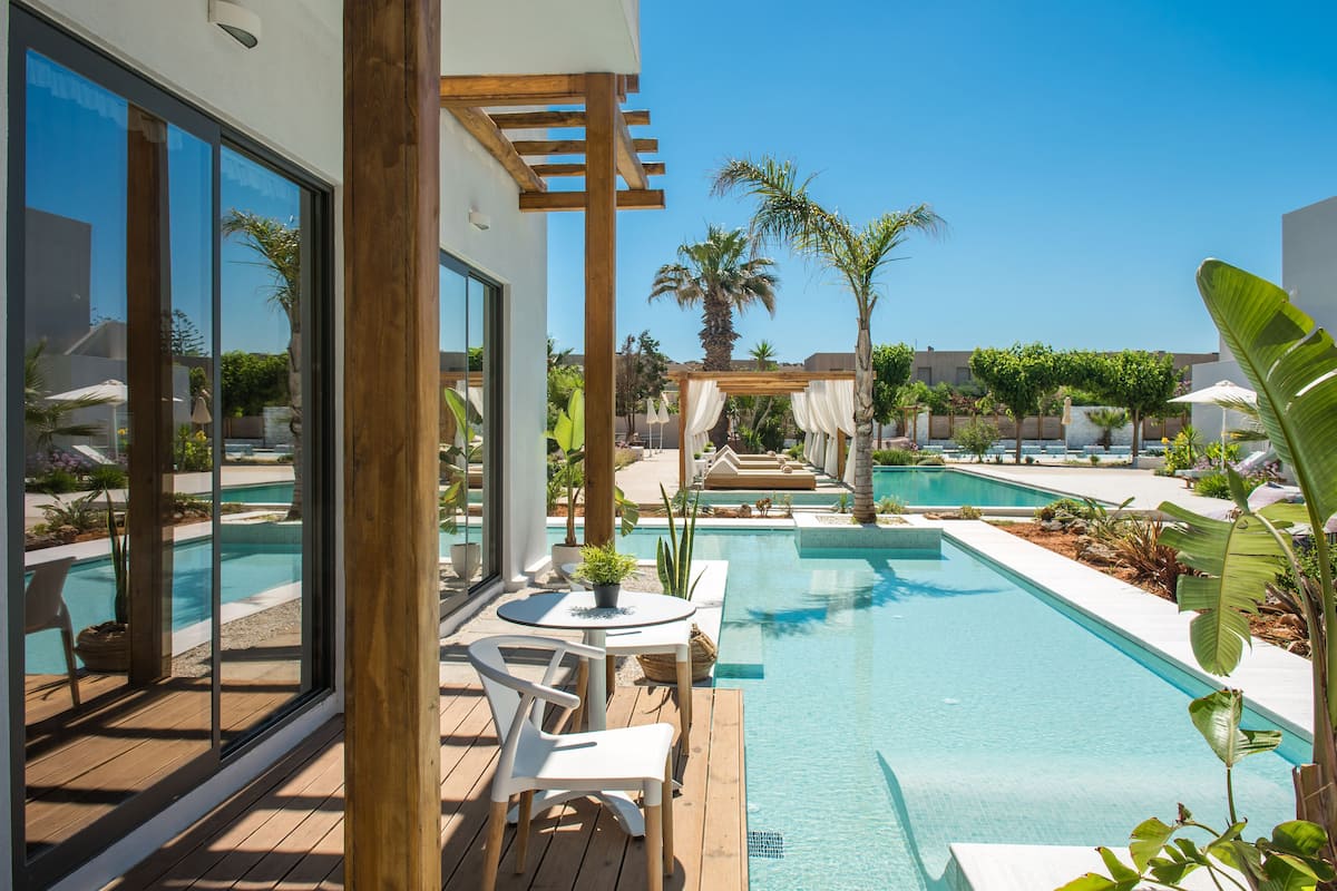 Ett poolområde med ett trädäck, vita stolar och en pergola.