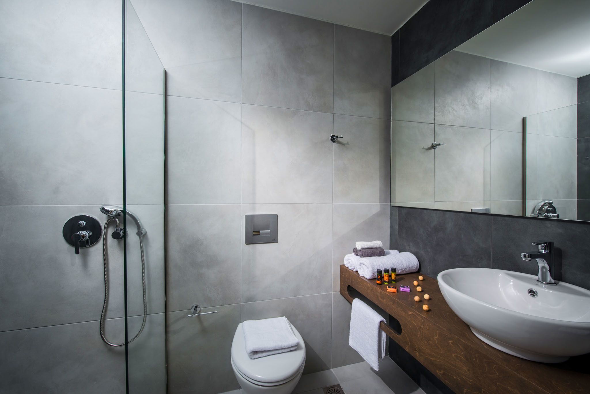 A modern bathroom with a glass shower enclosure, a white toilet, and a wooden vanity with a sink and mirror.