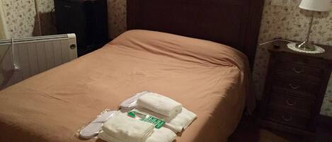 A neatly made bed with a brown bedspread, a set of white towels, and a folded green towel on the bed.