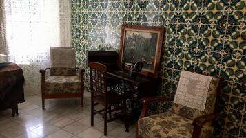 A room with two wooden chairs, a piano, and a patterned wall.