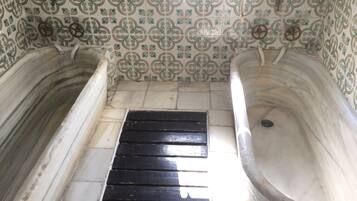 Une salle de bain avec deux baignoires en marbre, un drain noir et des murs recouverts de carreaux à motifs.