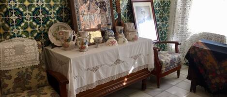 Una habitación con pared de azulejos, una mesa con adornos, un cuadro enmarco y muebles con estampado floral.