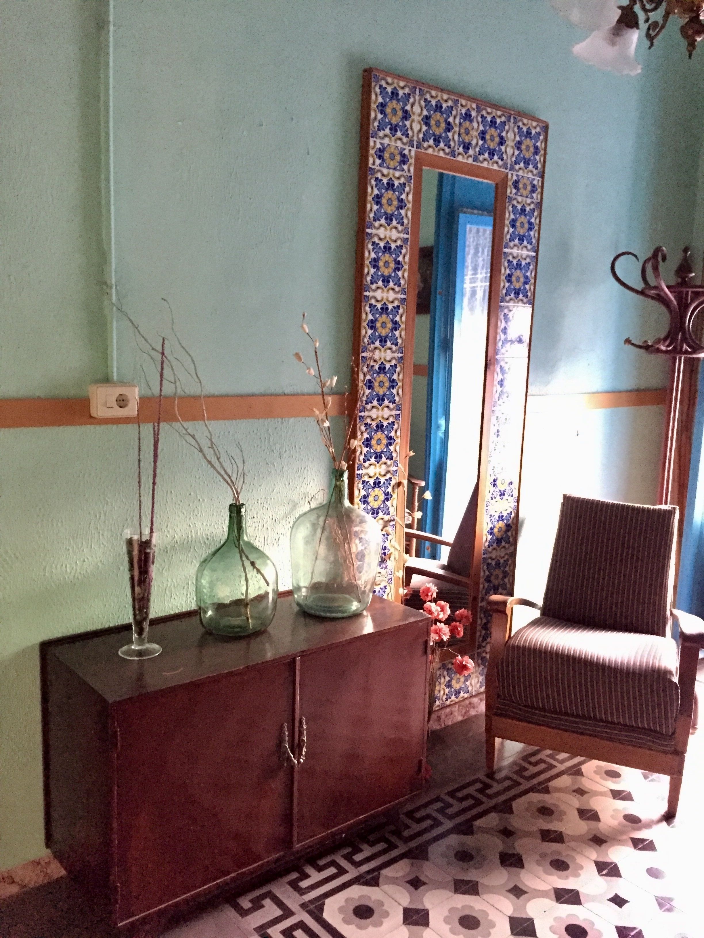A room with a wooden cabinet, a chair, and a mirror with a blue and white tile border.