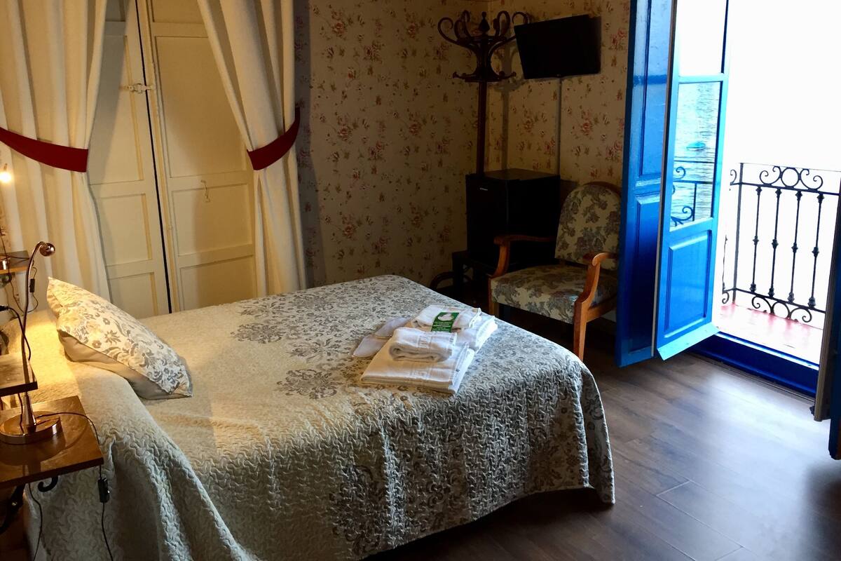 Un dormitorio con cama, una silla, televisor y ventana con vistas.