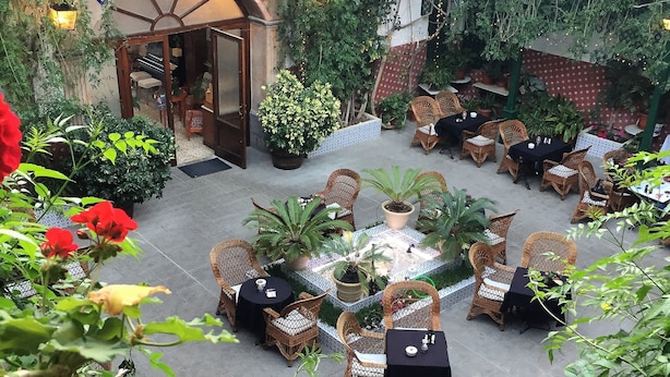 Une cour avec des sièges en plein air, des plantes en pot et une enseigne indiquant « BAINS THERMAUX ».
