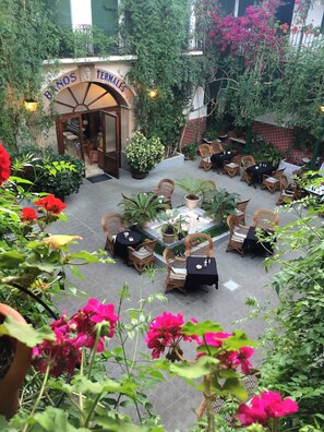 A courtyard with outdoor seating, potted plants, and a sign reading "BANOS TERMALES". - Balneario La Encarnación (Los Alcazares)
