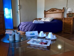 Habitación de hotel con una cama, una mesita de noche de madera, una mesa de vidrio con artículos de tocador y una puerta azul.