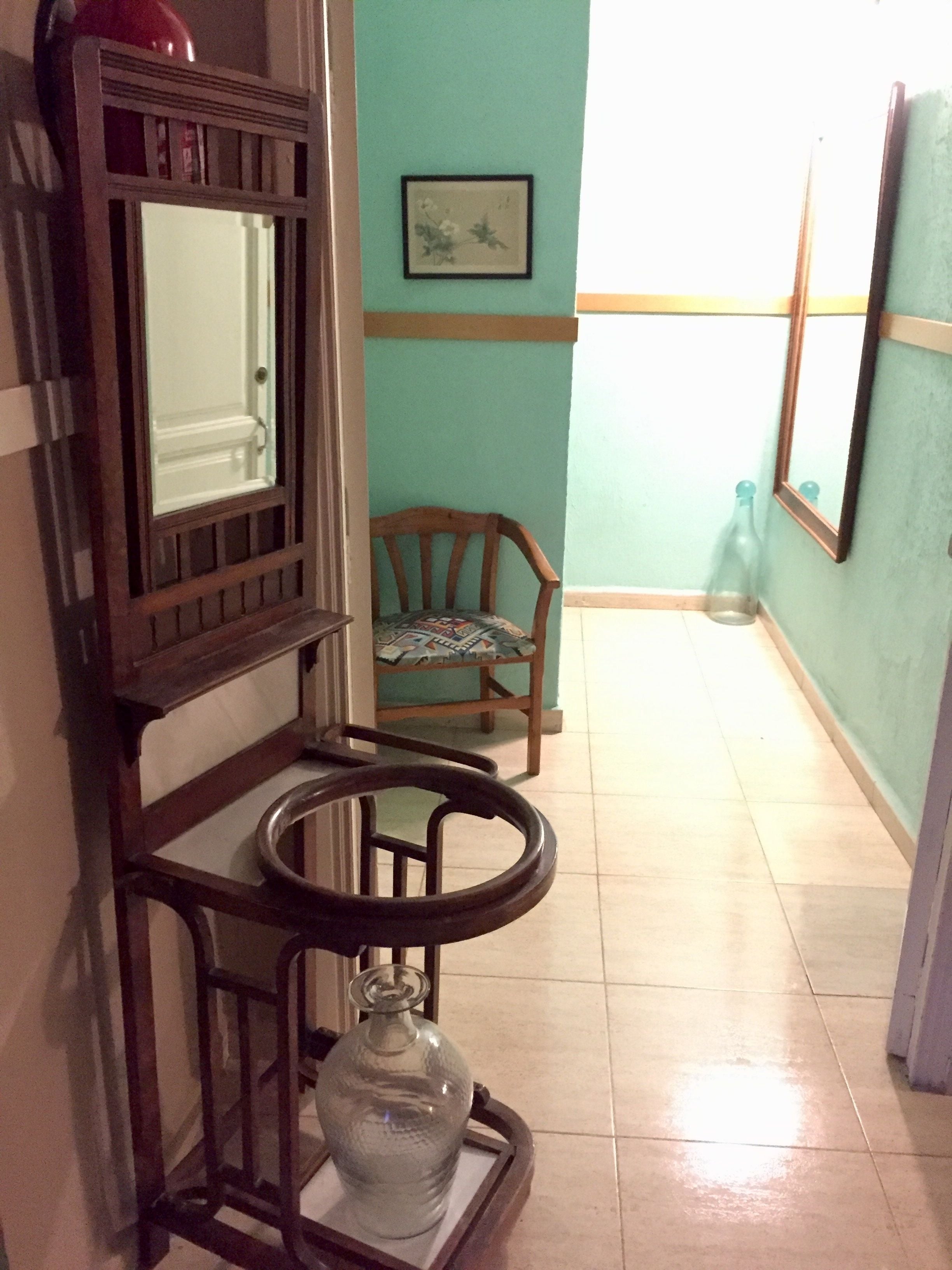 A hallway with a wooden bench, a glass vase, and a chair.