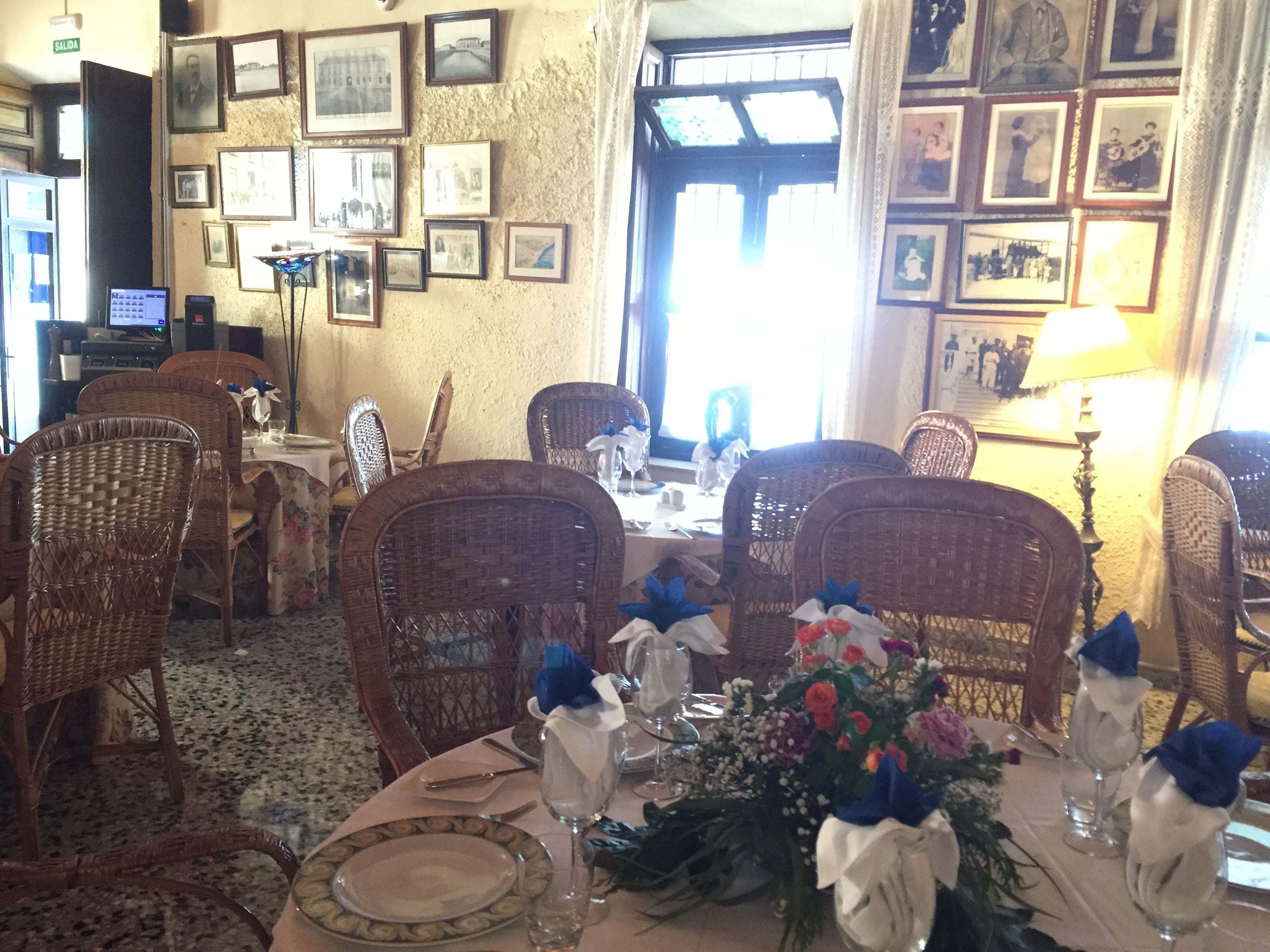 Un comedor con sillas de mimbre, una mesa lista para comer y cuadros en las paredes.