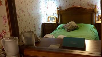 A hotel room with a bed, a nightstand, a mirror, and a bedside table with a kettle and a cup.