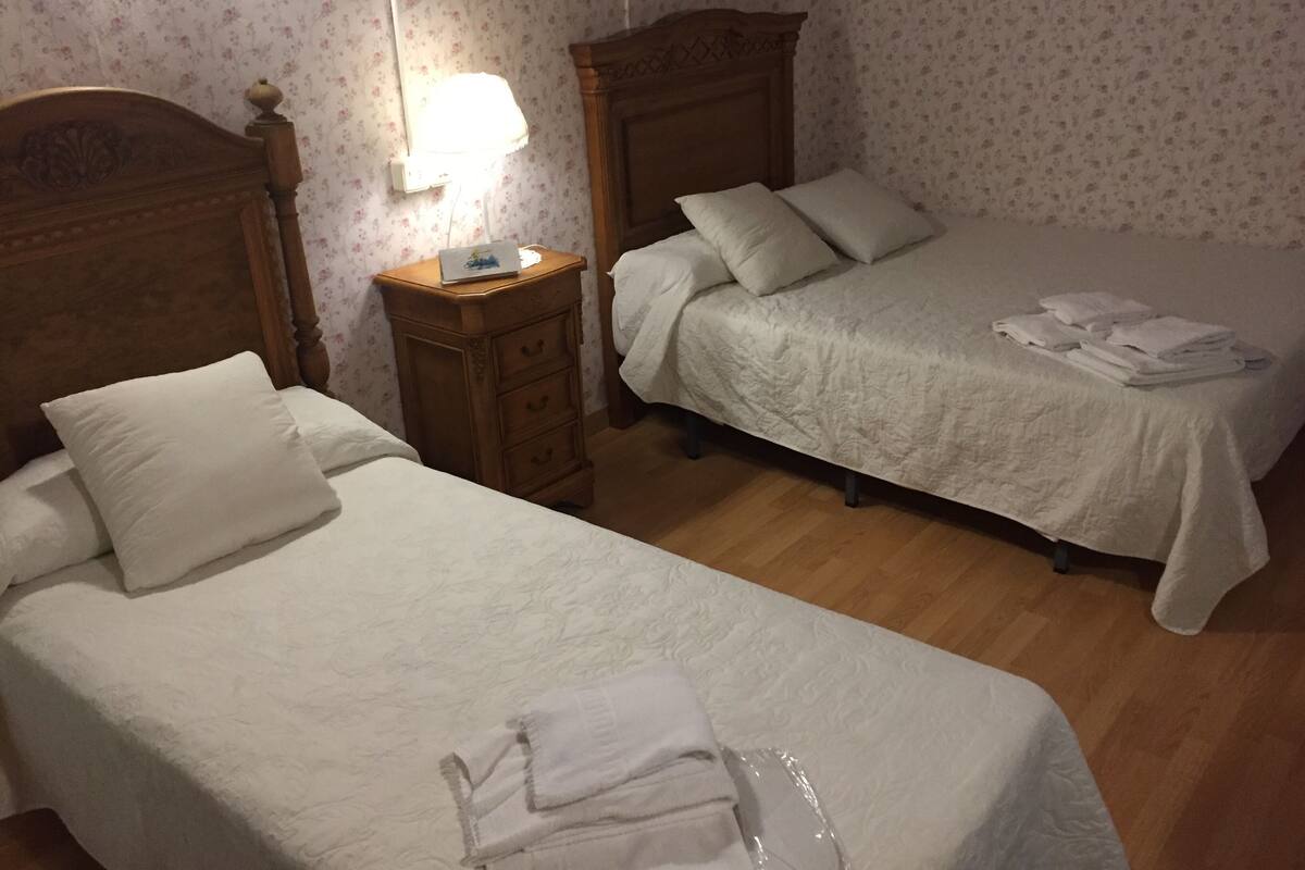 Un dormitorio con dos camas individuales, una mesita de noche de madera y una lámpara.