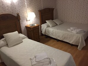 Un dormitorio con dos camas individuales, una mesita de noche de madera y una lámpara.