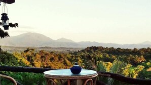 Ein Balkon mit Korbstühlen und einem Tisch, der auf eine gebirgige Landschaft mit dichter Vegetation blickt.