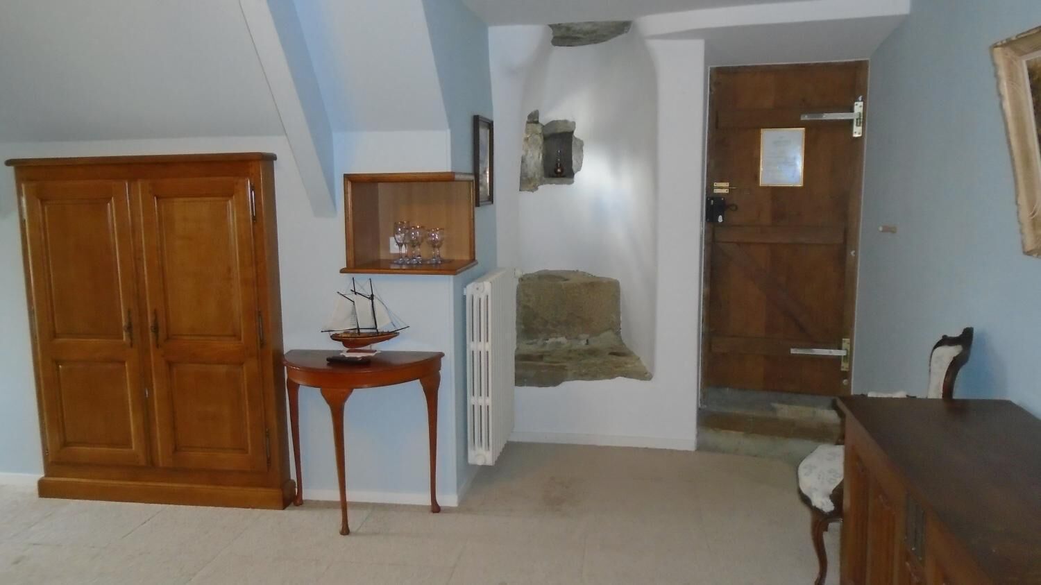 Een kamer met een houten garderobe, een klein tafeltje met een schipmodel, een plank met kristallen, een stenen muur en een houten deur.