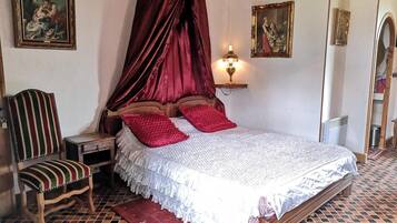 Une chambre à coucher avec un lit à baldaquin, une chaise en bois, une table de chevet et une lampe fixée au mur.