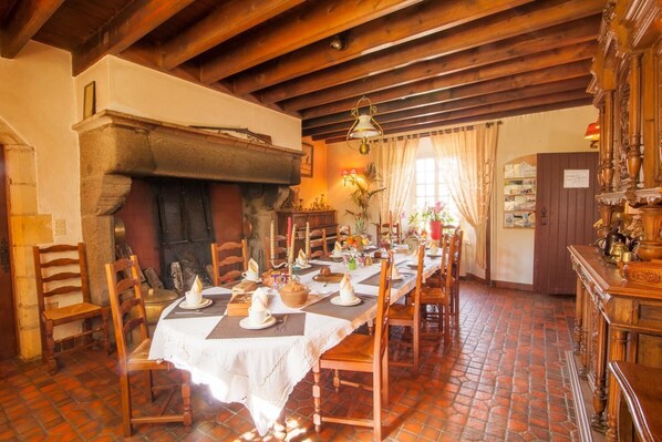 A dining room with a brick floor, wooden chairs, a table set with white tablecloths and candles, and a fireplace. - Logis le Manoir de la Foulerie (Saint-Sauveur-Villages)