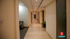 Un pasillo de hotel con diseño moderno, que presenta un largo pasillo con puertas a ambos lados, un banco a la izquierda y una planta a la derecha.