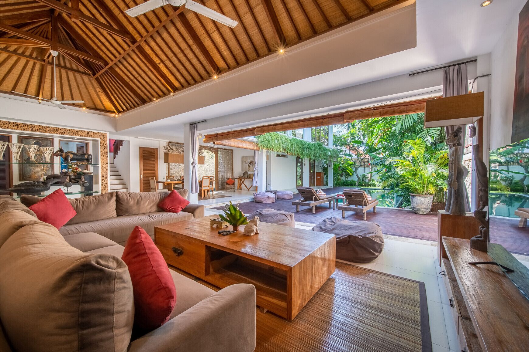 Un vaste espace de vie agrémenté d’un plafond en bois, d’un grand canapé, d’une table basse et offrant une vue sur un jardin luxuriant.