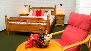 A wooden bed with a headboard, two bedside tables with lamps, a red chair, and a round table with a basket of fruit. - Mueritz Landhausperle (Röbel/Müritz)