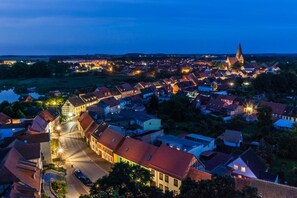 A town at dusk with illuminated buildings and a prominent church spire. - Mueritz Landhausperle (Röbel/Müritz)