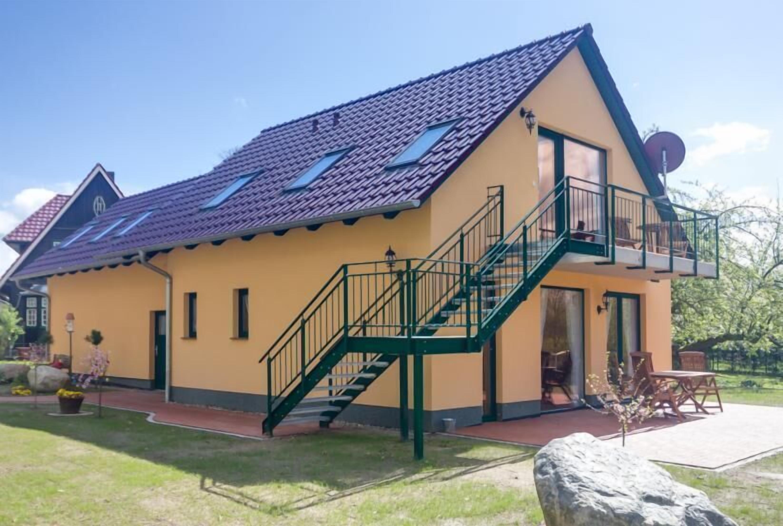 A two-story house with a tiled roof, a balcony with a green railing, and a satellite dish.