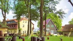 A courtyard with outdoor seating, surrounded by trees and buildings with varied architectural styles. - Mueritz Landhausperle (Röbel/Müritz)