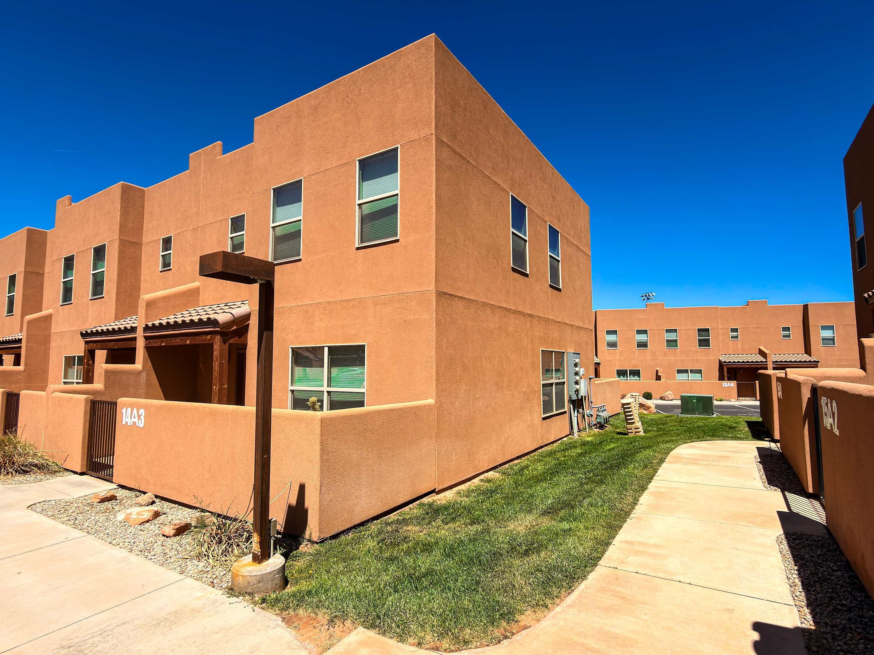A modern building with a flat roof, multiple windows, and a paved walkway.