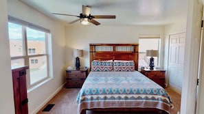 A bedroom with a bed, a ceiling fan, two bedside tables with lamps, a window, and a door.