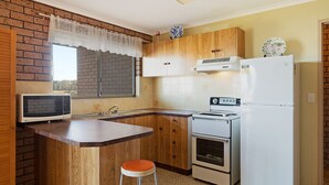 Eine kompakte Küche mit Holzausstattung, einer integrierten Mikrowelle, einem Toaster und einem Kühlschrank.