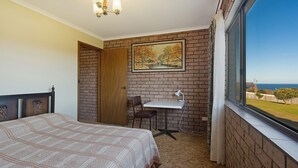 Ein Schlafzimmer mit Bett, Schreibtisch und Stuhl. An der Wand hängt ein Gemälde und das Fenster bietet Blick aufs Meer.