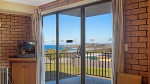 Ein Zimmer mit einer großen Schiebeglasdoor, die auf einen Balkon mit Meerblick und in der Ferne Gebäuden führt.