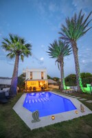 Una casa moderna con piscina, palmeras y mobiliario exterior.