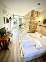 Habitación de hotel con cama, escritorio con computadora, baño con espejo y vista al exterior.