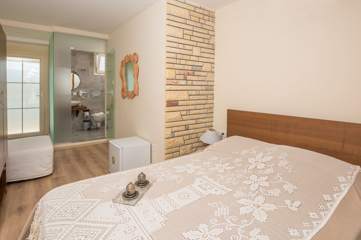 Ein Schlafzimmer mit einem großen Bett, einem Holzkopfende, einer Wand aus Stein, einem Spiegel und Blick ins Badezimmer.
