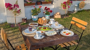 Een buitentafel gedekt met borden, brood en een salade, omringd door plantenpotten en een houten bankje.
