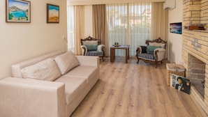 Een woonkamer met een beige bank, twee fauteuils, een bijzettafeltje en een open haard.