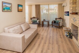 Un salón con un sofá color beige, dos sillones tapizados, una mesita y una chimenea.