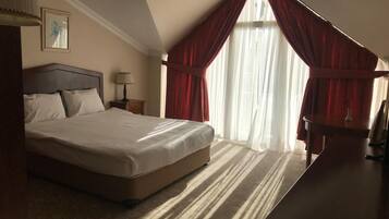 Una habitación de hotel con una cama grande, un escritorio y una ventana con cortinas rojas.