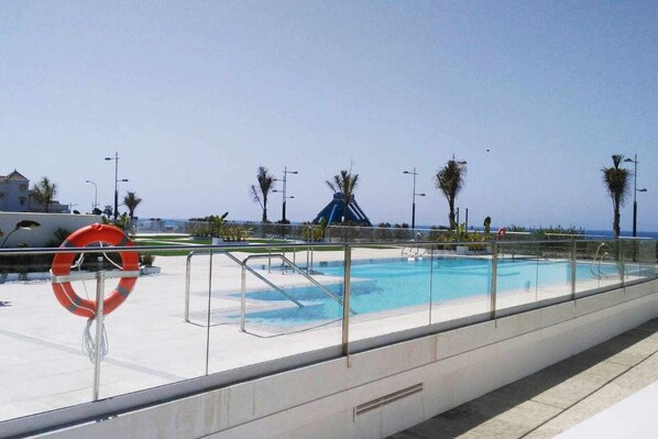 A swimming pool with a glass railing, a lifebuoy, and a water slide in the background. - Panorama Beach Apartment - Torrox Costa (Torrox-Costa)