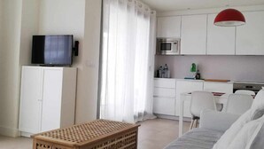 A modern living room with a TV, a wooden crate, a sofa, and a kitchen area with a microwave and cabinets. - Panorama Beach Apartment - Torrox Costa (Torrox-Costa)