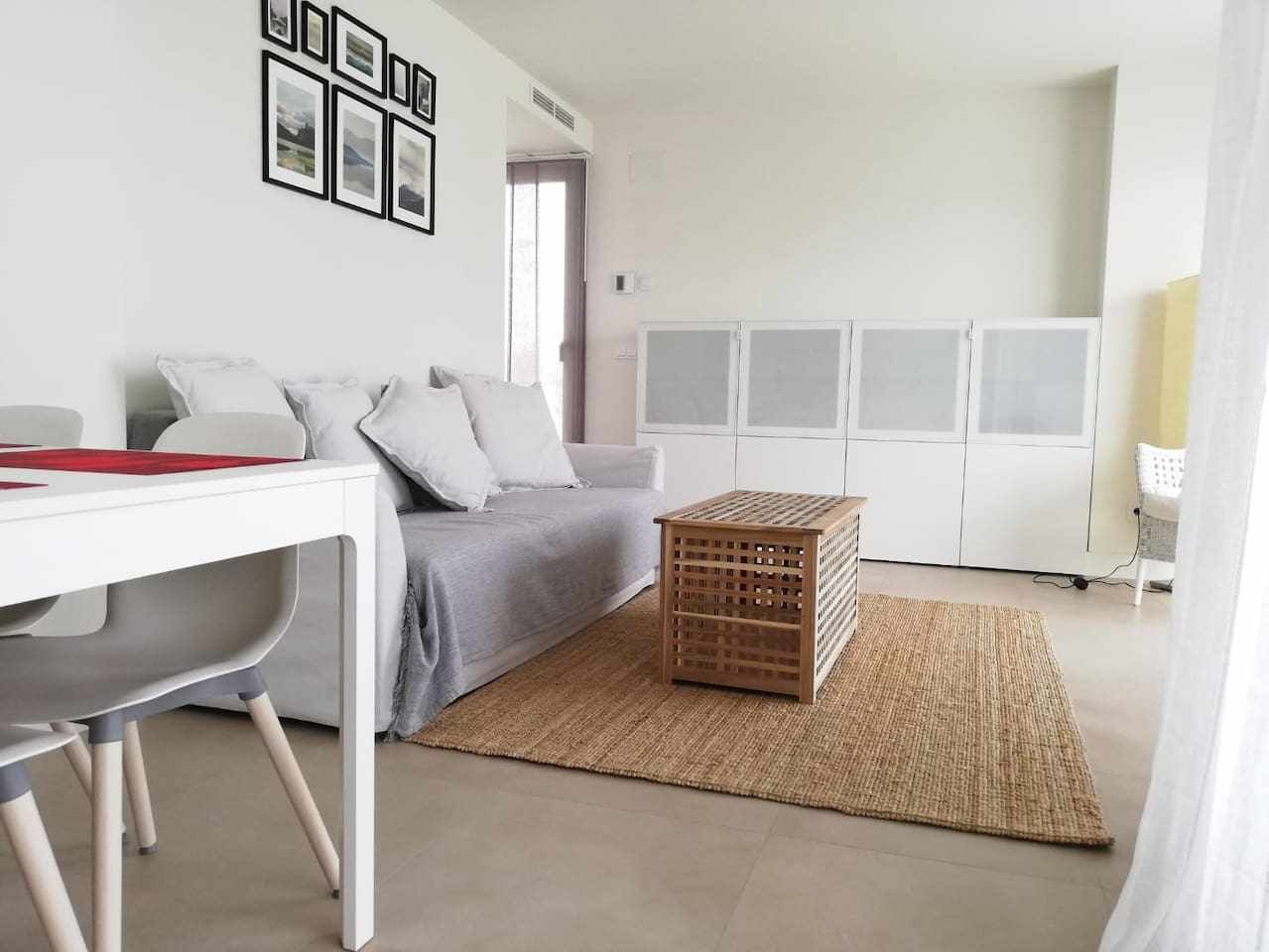 A modern living room with a white sofa, a dining table, and a small wooden side table.