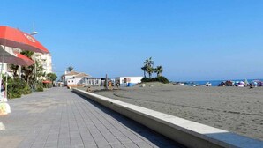 A paved walkway leading to a beach with umbrellas and palm trees. - Panorama Beach Apartment - Torrox Costa (Torrox-Costa)