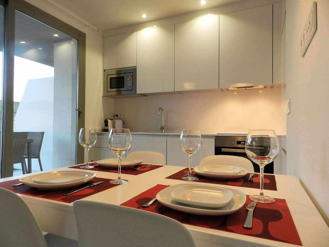 A dining area with a table set for four, equipped with wine glasses and plates, in a modern kitchen with white cabinets and a microwave.