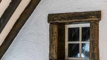 Een rustieke kamer met een klein raam, houten balken en witte wanden.