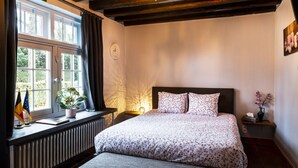 A bedroom with a large bed, a window with curtains, a bedside table with a lamp, and a radiator. - Rose House B&B (Ghent)