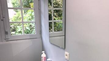 Een badkamer met een witte wastafel, een spiegel, een raam en een handdoekhouder.