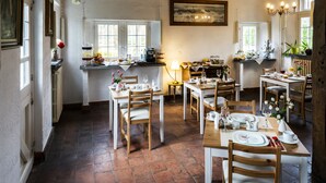 A dining area with multiple tables set for meals, wooden chairs, and a rustic interior with exposed beams and tiled floors. - Rose House B&B (Ghent)