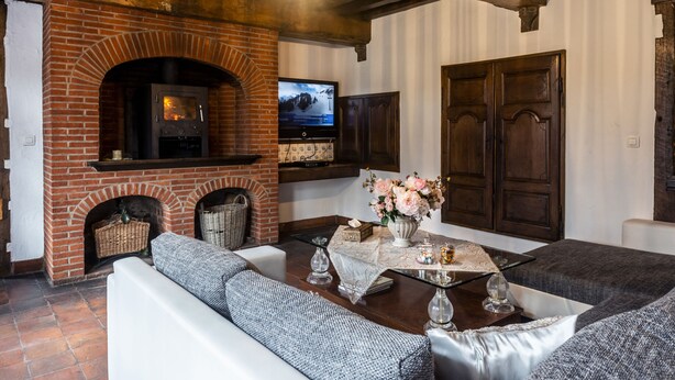 A cozy living room with a brick fireplace, a television mounted above it, and comfortable seating. - Rose House B&B (Ghent)