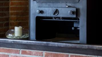 A wood-burning stove with a glass door, a control panel, and a brick chimney.